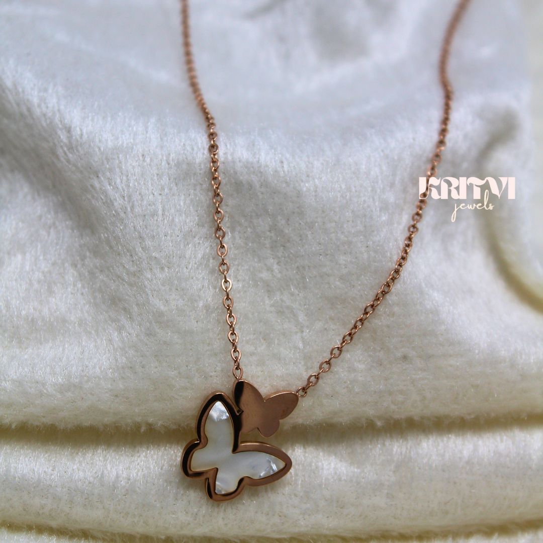 Rose gold-toned necklace featuring a butterfly pendant with a white inlay on one of the butterfly’s wings